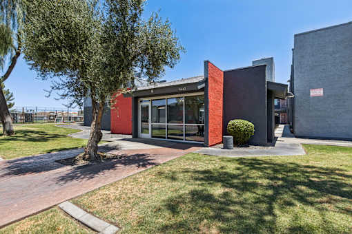 A modern building with a red and grey exterior is surrounded by a grassy area and a tree.