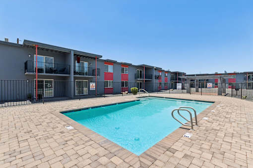 A swimming pool surrounded by a brick patio and apartment buildings.