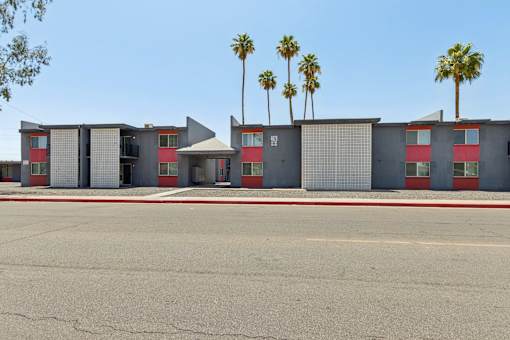 A building with a red and grey facade and palm trees in the background.