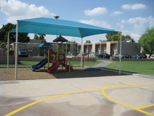 a playground with a canopy and slides in front of a building