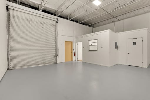 a large empty room with a garage door and a door to a hallway