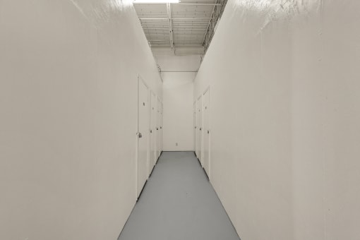 a long hallway with white walls and doors and a gray floor