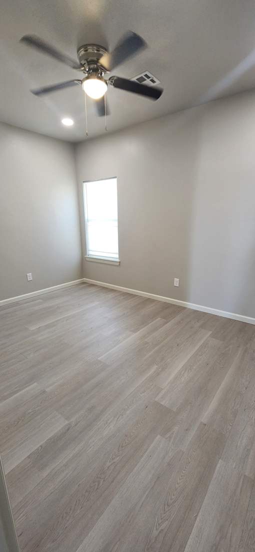 A ceiling fan is mounted on the wall in a room with light wood flooring and a skylight.