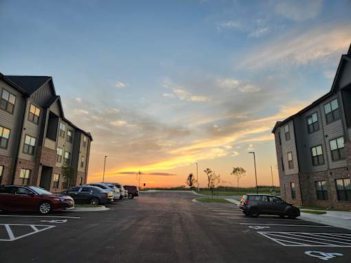 A parking lot with cars parked and buildings on either side during sunset.