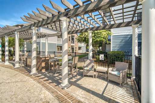 A patio with a white pergola and chairs.