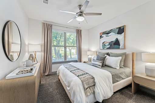 A bedroom with a large bed, a ceiling fan, and a painting on the wall.