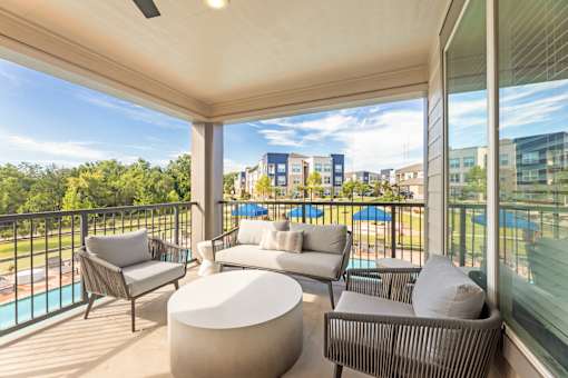 A balcony with a white couch, grey armchair, and a white ottoman.