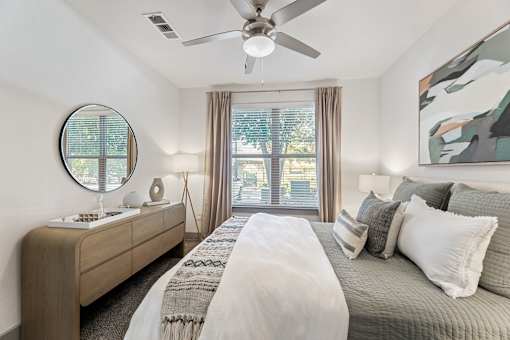 A bedroom with a large bed, a mirror, and a ceiling fan.