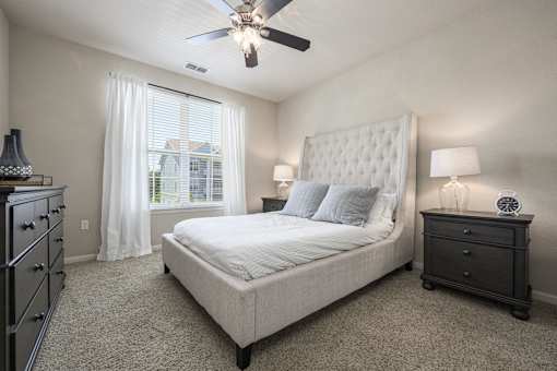A bedroom with a large bed, a dresser, and a ceiling fan.