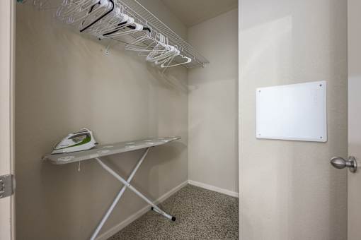 A white ironing board with clothes hangers on the wall.