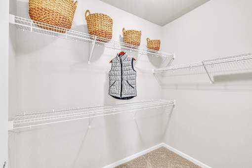 A grey vest hanging on a white shelf with two wicker baskets above it.