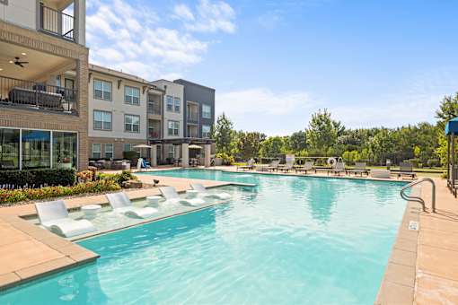 A large swimming pool with lounge chairs and apartment buildings in the background.