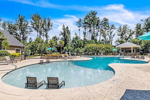 A swimming pool surrounded by trees and chairs.
