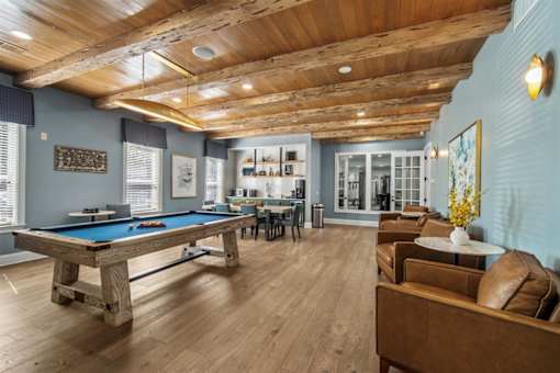 A pool table is surrounded by leather chairs in a room with wooden floors and ceiling.