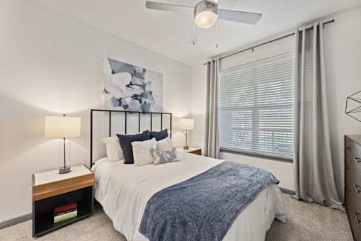 A bedroom with a bed, two lamps, and a painting on the wall.
