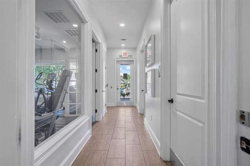 A long hallway with white doors and a red exit sign.