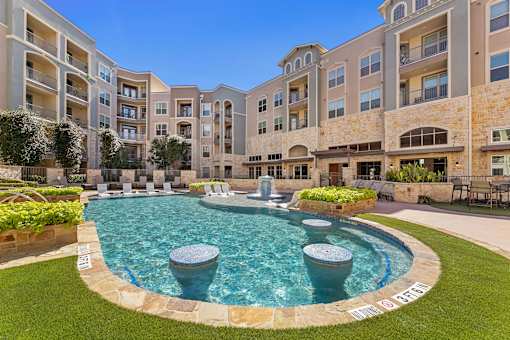 A large swimming pool surrounded by a stone border in a courtyard.