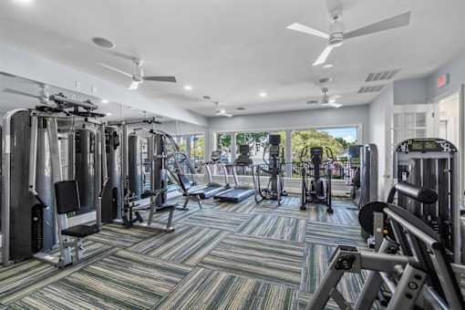 A gym with a variety of equipment including treadmills, weights, and a ceiling fan.