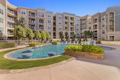 A swimming pool surrounded by a grassy area and apartment buildings.