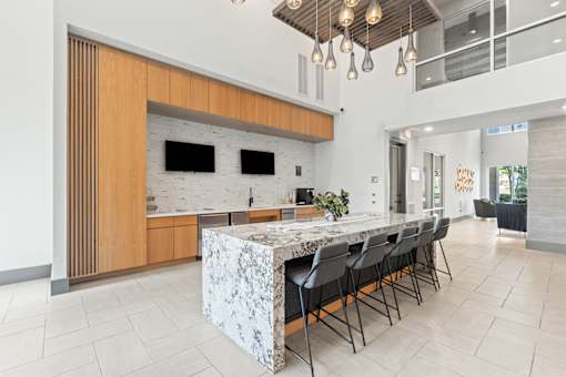 A modern kitchen with a marble island and black chairs.