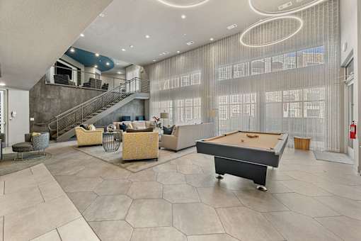 A billiard table is in the middle of a spacious room with a staircase and a fire extinguisher.