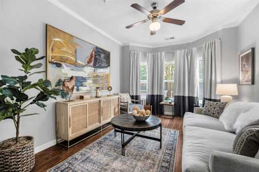 A living room with a ceiling fan, a large painting, a wooden cabinet, a coffee table, and a potted plant.