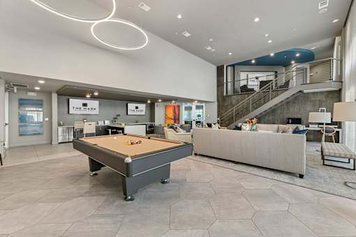 A billiard table is in the middle of a spacious room with a couch and a staircase.