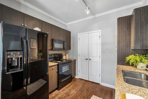 A kitchen with a black fridge, white cabinets, and a wooden floor.
