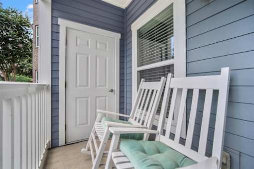 A white chair is placed on a green cushion on a porch.
