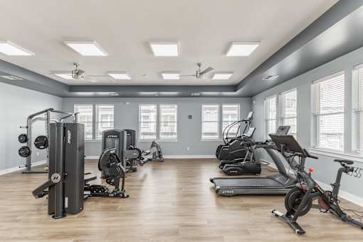 A spacious gym with a variety of equipment including treadmills, stationary bikes, and weight machines at Prosper Madison Oaks, Madison, AL
