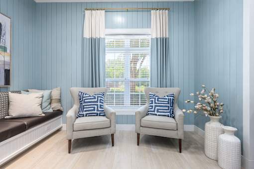 Two chairs with blue and white pillows in front of a window.