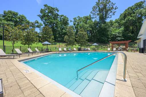A large outdoor swimming pool surrounded by trees and lounge chairs.