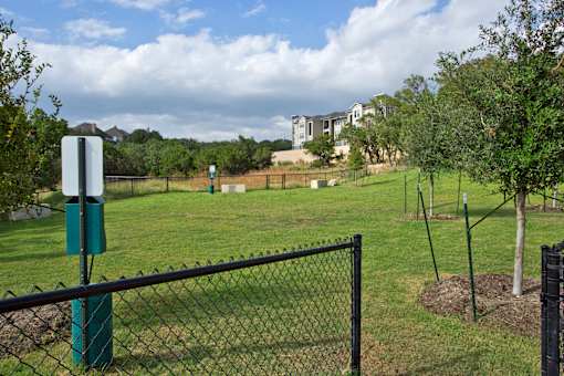 A green sign on a pole stands in a grassy field behind a black fence.