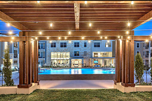 A pool surrounded by a wooden pergola with lights on it.
