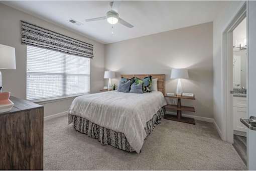 A bedroom with a bed, two lamps, and a window with blinds at Waterleaf at Neely Ferry Apartments, Simpsonville, 29680