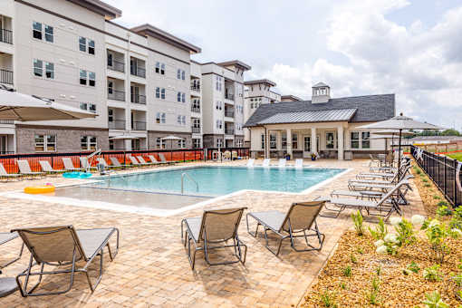 A pool surrounded by chairs and umbrellas in front of a building.