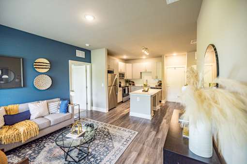 A living room with a couch, coffee table, and a kitchen area in the background.
