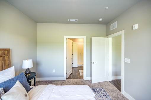 A bedroom with a bed, nightstand, and a doorway leading to another room.