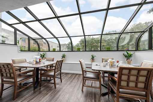 A glass roofed room with wooden chairs and tables.