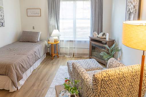 A bedroom with a bed, a chair, and a nightstand with a lamp.