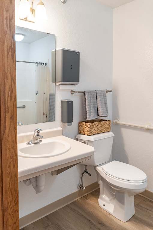 A bathroom with a toilet, sink, mirror, and towel rack.