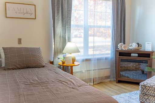 A bedroom with a bed, nightstand, and a window with curtains.