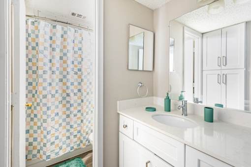 A bathroom with a checkered shower curtain and white cabinets.