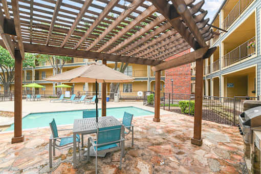 A patio with a table and chairs under a wooden pergola.