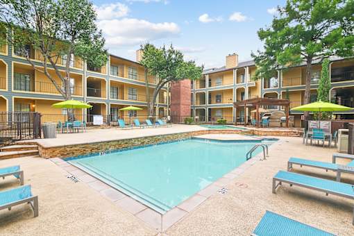 A swimming pool surrounded by apartment buildings and lounge chairs.