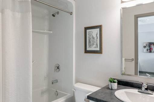 A bathroom with a white tub, sink, and a picture on the wall.