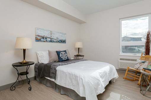 A bedroom with a bed, two lamps, and a painting on the wall.