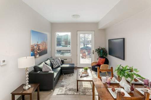 A living room with a black couch, a wooden coffee table, and a large window.