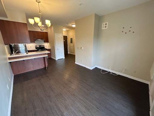 A kitchen with dark wood floors and a white wall.