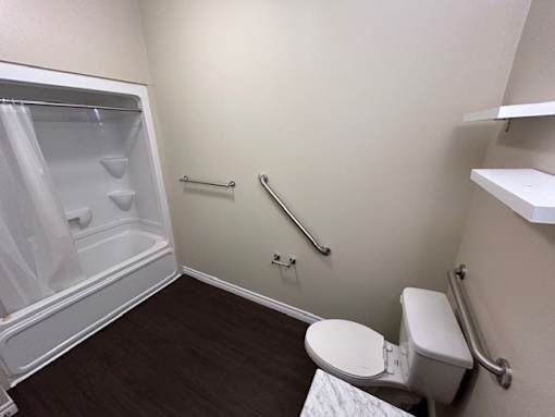 A small bathroom with a toilet, a shower with a glass door, and a grab bar.